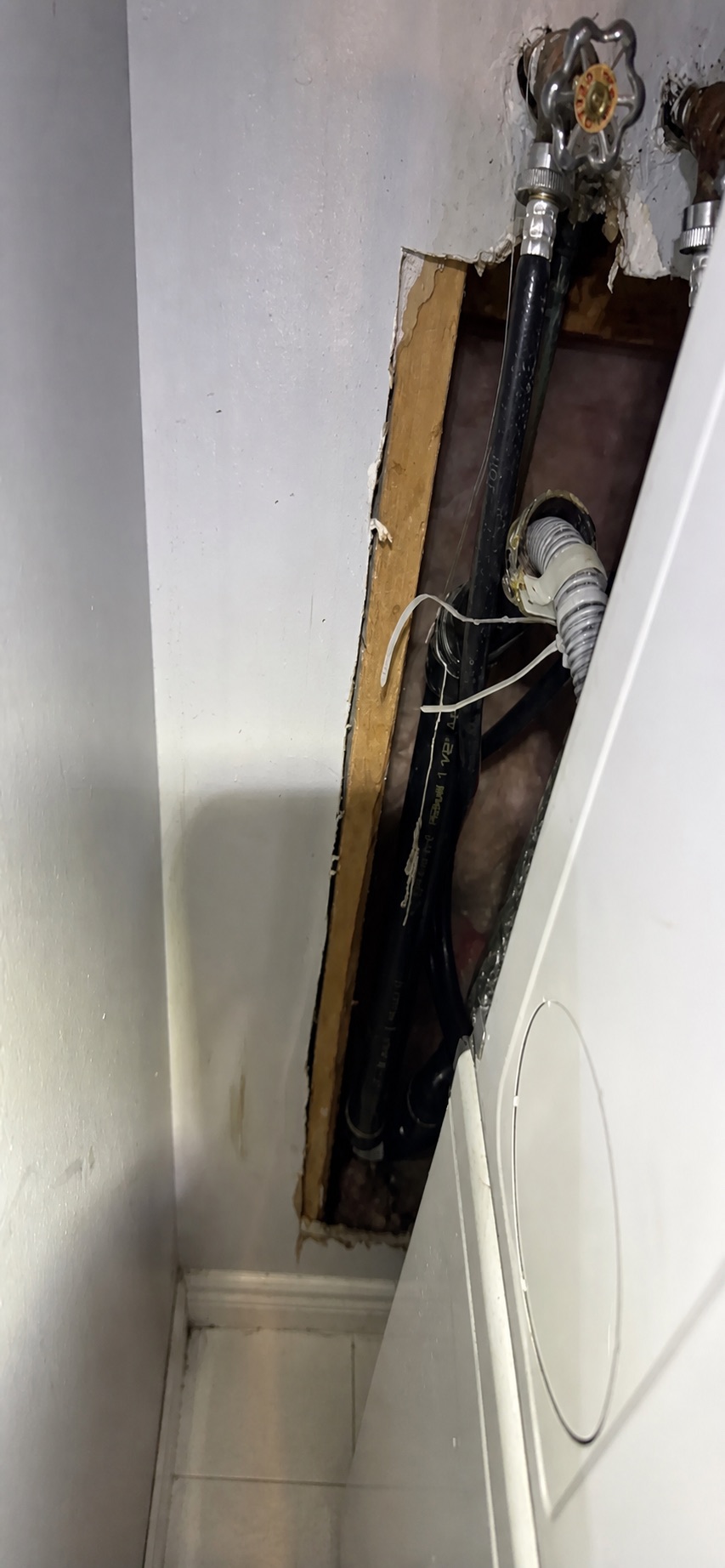 Customer-supplied wide photo showing a washing machine beside an open wall area with laundry supply and drain connections